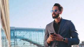 Άποψη περιστροφής του ελκυστικού ατόμου σε ένα κοστούμι χρησιμοποιώντας το κινητό τηλέφωνο του και χαμογελώντας ευτυχώς, που κοιτ απόθεμα βίντεο Άποψη περιστροφής του ελκυστικού ατόμου σε ένα κοστούμι χρησιμοποιώντας το κινητό τηλέφωνο του και χαμογελώντας ευτυχώς, που κοιτ απόθεμα βίντεο