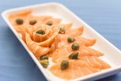 Άσπρο πιάτο με sashimi σολομών και κάπαρες στο μπλε υπόβαθρο στοκ εικόνα με δικαίωμα ελεύθερης χρήσης Άσπρο πιάτο με sashimi σολομών και κάπαρες στο μπλε υπόβαθρο στοκ εικόνα με δικαίωμα ελεύθερης χρήσης