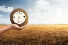 Άτομο που κρατά ένα ρολόι με το ξηρό υπόβαθρο τομέων χλόης Στοκ Εικόνα Άτομο που κρατά ένα ρολόι με το ξηρό υπόβαθρο τομέων χλόης Στοκ Εικόνα