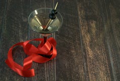 Ένα martini γυαλί με μια ελιά και ερυθρά κορδέλλα σε έναν ξύλινο πίνακα στοκ εικόνα με δικαίωμα ελεύθερης χρήσης Ένα martini γυαλί με μια ελιά και ερυθρά κορδέλλα σε έναν ξύλινο πίνακα στοκ εικόνα με δικαίωμα ελεύθερης χρήσης