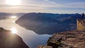 Ένα άτομο που στέκεται στο διάσημο βράχο Preikestolen στη Νορβηγία Η ανατολή πραγματοποιείται πέρα από το φιορδ στοκ εικόνες με δικαίωμα ελεύθερης χρήσης Ένα άτομο που στέκεται στο διάσημο βράχο Preikestolen στη Νορβηγία Η ανατολή πραγματοποιείται πέρα από το φιορδ στοκ εικόνες με δικαίωμα ελεύθερης χρήσης