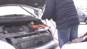 Ένα άτομο συνδέει τα υψηλής τάσεως καλώδια από ένα αυτοκίνητο χορηγών για τη φόρτιση μιας μηχανής αυτοκινήτων με μια απαλλαγμένη απόθεμα βίντεο Ένα άτομο συνδέει τα υψηλής τάσεως καλώδια από ένα αυτοκίνητο χορηγών για τη φόρτιση μιας μηχανής αυτοκινήτων με μια απαλλαγμένη απόθεμα βίντεο