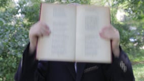 Ένα αγόρι με ένα βιβλίο στα χέρια του που παίζουν το πρόσωπό του Το αγόρι φαίνεται αστείο από πίσω από το βιβλίο Το αγόρι στο σακ απόθεμα βίντεο Ένα αγόρι με ένα βιβλίο στα χέρια του που παίζουν το πρόσωπό του Το αγόρι φαίνεται αστείο από πίσω από το βιβλίο Το αγόρι στο σακ απόθεμα βίντεο