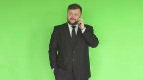 Ένα καυκάσιο άτομο σε ένα μαύρο επιχειρησιακό κοστούμι με μια γενειάδα λύνει τα προβλήματα τηλεφωνικώς στο υπόβαθρο ενός πράσινου φιλμ μικρού μήκους Ένα καυκάσιο άτομο σε ένα μαύρο επιχειρησιακό κοστούμι με μια γενειάδα λύνει τα προβλήματα τηλεφωνικώς στο υπόβαθρο ενός πράσινου φιλμ μικρού μήκους