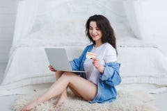 Ένα κορίτσι με ένα lap-top και μια τραπεζική κάρτα κάθεται στο κρεβάτι και εξετάζει την στοκ εικόνες Ένα κορίτσι με ένα lap-top και μια τραπεζική κάρτα κάθεται στο κρεβάτι και εξετάζει την στοκ εικόνες