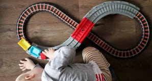 Ένα μικρό αγόρι παίζει έναν σιδηρόδρομο των παιδιών Το Mom προσέχει το γιο της άνωθεν Το παιδί συναρπάζεται με το τραίνο στοκ εικόνες Ένα μικρό αγόρι παίζει έναν σιδηρόδρομο των παιδιών Το Mom προσέχει το γιο της άνωθεν Το παιδί συναρπάζεται με το τραίνο στοκ εικόνες