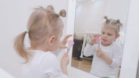 Ένα μικρό κορίτσι μπροστά από έναν καθρέφτη ισχύει makeup στο πρόσωπό της με μια βούρτσα χαριτωμένο κορίτσι λίγο πορτρέτο απόθεμα βίντεο Ένα μικρό κορίτσι μπροστά από έναν καθρέφτη ισχύει makeup στο πρόσωπό της με μια βούρτσα χαριτωμένο κορίτσι λίγο πορτρέτο απόθεμα βίντεο