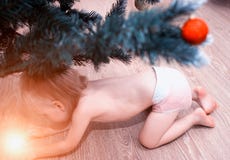 Ένα μικρό παιδί σε μια πάνα κοιτάζει κάτω από το καμμένος θαυμάσιο δώρο δέντρων, μαγικό για το νέο έτος, παραμύθι, χαμόγελο στοκ εικόνες Ένα μικρό παιδί σε μια πάνα κοιτάζει κάτω από το καμμένος θαυμάσιο δώρο δέντρων, μαγικό για το νέο έτος, παραμύθι, χαμόγελο στοκ εικόνες