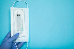 Ένα μπλε-φορημένο γάντια χέρι κρατά μια αποστειρωμένες σύριγγα και μια μάσκα Ανοσοποίηση r στοκ φωτογραφία Ένα μπλε-φορημένο γάντια χέρι κρατά μια αποστειρωμένες σύριγγα και μια μάσκα Ανοσοποίηση r στοκ φωτογραφία