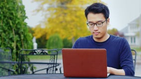 Ένα νέο ασιατικό άτομο εργάζεται με ένα lap-top Να καθίσει υπαίθρια σε μια χαρακτηριστική αμερικανική πόλη Ένα νέο ασιατικό άτομο εργάζεται με ένα lap-top Να καθίσει υπαίθρια σε μια χαρακτηριστική αμερικανική πόλη