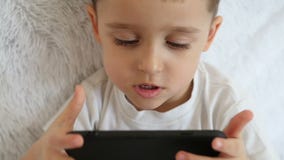 Ένα παιδί κρατά ένα smartphone μπροστά από τον και παίζει τα παιχνίδια σε σε αργή κίνηση σε ένα άσπρο υπόβαθρο φιλμ μικρού μήκους Ένα παιδί κρατά ένα smartphone μπροστά από τον και παίζει τα παιχνίδια σε σε αργή κίνηση σε ένα άσπρο υπόβαθρο φιλμ μικρού μήκους