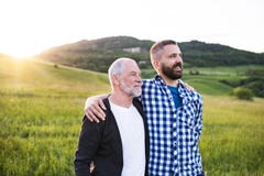 Ένα πορτρέτο ενός ενήλικου γιου hipster με τον ανώτερο πατέρα στη φύση στο ηλιοβασίλεμα, όπλα η μια γύρω από την άλλη στοκ εικόνα με δικαίωμα ελεύθερης χρήσης Ένα πορτρέτο ενός ενήλικου γιου hipster με τον ανώτερο πατέρα στη φύση στο ηλιοβασίλεμα, όπλα η μια γύρω από την άλλη στοκ εικόνα με δικαίωμα ελεύθερης χρήσης
