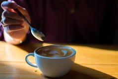 Ένα χέρι κρατά ένα κουτάλι για να δοκιμάσει latte τον καφέ στοκ φωτογραφία με δικαίωμα ελεύθερης χρήσης Ένα χέρι κρατά ένα κουτάλι για να δοκιμάσει latte τον καφέ στοκ φωτογραφία με δικαίωμα ελεύθερης χρήσης