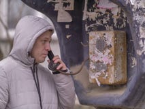 Ένας νεαρός άνδρας σε ένα σακάκι με μια κουκούλα μιλά σε έναν παλαιό κερματοδέκτη στην οδό στοκ φωτογραφία με δικαίωμα ελεύθερης χρήσης Ένας νεαρός άνδρας σε ένα σακάκι με μια κουκούλα μιλά σε έναν παλαιό κερματοδέκτη στην οδό στοκ φωτογραφία με δικαίωμα ελεύθερης χρήσης