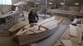 Ένας ξυλουργός γυαλίζει την ξύλινη βάρκα λεπτομερειών στο ναυπηγείο απόθεμα βίντεο Ένας ξυλουργός γυαλίζει την ξύλινη βάρκα λεπτομερειών στο ναυπηγείο απόθεμα βίντεο