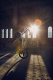 Ακροβατική επίδειξη BMX και οδήγηση άλματος σε μια αίθουσα με το φως του ήλιου στοκ εικόνα Ακροβατική επίδειξη BMX και οδήγηση άλματος σε μια αίθουσα με το φως του ήλιου στοκ εικόνα