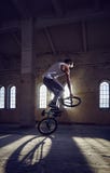 Ακροβατική επίδειξη BMX και οδήγηση άλματος σε μια αίθουσα με το φως του ήλιου στοκ εικόνες με δικαίωμα ελεύθερης χρήσης Ακροβατική επίδειξη BMX και οδήγηση άλματος σε μια αίθουσα με το φως του ήλιου στοκ εικόνες με δικαίωμα ελεύθερης χρήσης