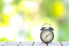 Αναδρομικό μαύρο ξυπνητήρι στον ξύλινο πίνακα στοκ φωτογραφία με δικαίωμα ελεύθερης χρήσης Αναδρομικό μαύρο ξυπνητήρι στον ξύλινο πίνακα στοκ φωτογραφία με δικαίωμα ελεύθερης χρήσης