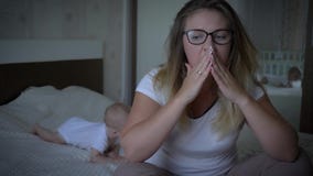 Ανατρέψτε το νέο mum κάθεται στην άκρη του κρεβατιού στο υπόβαθρο του σερνμένος μωρού στο σπίτι απόθεμα βίντεο Ανατρέψτε το νέο mum κάθεται στην άκρη του κρεβατιού στο υπόβαθρο του σερνμένος μωρού στο σπίτι απόθεμα βίντεο