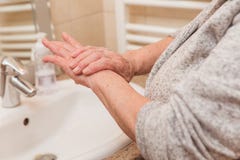 Ανώτερη γυναίκα στο μπουρνούζι που εφαρμόζει την κρέμα χεριών στο λουτρό, κινηματογράφηση σε πρώτο πλάνο στοκ εικόνα Ανώτερη γυναίκα στο μπουρνούζι που εφαρμόζει την κρέμα χεριών στο λουτρό, κινηματογράφηση σε πρώτο πλάνο στοκ εικόνα