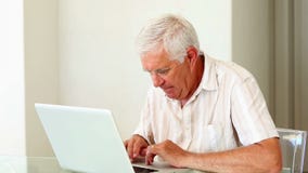 Ανώτερο άτομο που χρησιμοποιεί το lap-top στον πίνακα απόθεμα βίντεο Ανώτερο άτομο που χρησιμοποιεί το lap-top στον πίνακα απόθεμα βίντεο