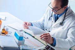 Ανώτερος αρσενικός γιατρός που ψάχνει τις πληροφορίες σε ένα ιατρικό βιβλίο στοκ εικόνες Ανώτερος αρσενικός γιατρός που ψάχνει τις πληροφορίες σε ένα ιατρικό βιβλίο στοκ εικόνες