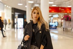 Αρκετά μοντέρνη νέα γυναίκα με τα ξανθά μαλλιά σε ένα καθιερώνον τη μόδα γκρίζο παλτό με μια μοντέρνη τσάντα δέρματος σε μια μοντ στοκ εικόνα Αρκετά μοντέρνη νέα γυναίκα με τα ξανθά μαλλιά σε ένα καθιερώνον τη μόδα γκρίζο παλτό με μια μοντέρνη τσάντα δέρματος σε μια μοντ στοκ εικόνα