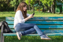 Αρκετά νέα γυναίκα που χρησιμοποιεί τη συνεδρίαση smartphone στον πάγκο Στοκ Εικόνες Αρκετά νέα γυναίκα που χρησιμοποιεί τη συνεδρίαση smartphone στον πάγκο Στοκ Εικόνες