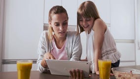 Αρκετά νέα μητέρα και η κόρη της που χρησιμοποιούν την ψηφιακή ταμπλέτα ενώ έχοντας το πρόγευμα στην κουζίνα στο σπίτι Αρκετά νέα μητέρα και η κόρη της που χρησιμοποιούν την ψηφιακή ταμπλέτα ενώ έχοντας το πρόγευμα στην κουζίνα στο σπίτι