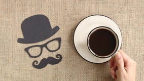 Αρσενικό σχέδιο σκιαγραφιών με το mustache, τα γυαλιά και το καπέλο με το φλιτζάνι του καφέ στο burlap υπόβαθρο Αρσενικό σχέδιο σκιαγραφιών με το mustache, τα γυαλιά και το καπέλο με το φλιτζάνι του καφέ στο burlap υπόβαθρο