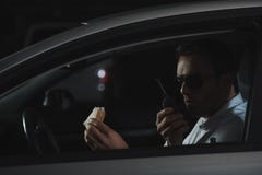 αρσενικός μυστικός αξιωματούχος στα γυαλιά ηλίου που έχουν το μεσημεριανό γεύμα και που χρησιμοποιούν την ομιλούσα ταινία walkie στοκ φωτογραφίες αρσενικός μυστικός αξιωματούχος στα γυαλιά ηλίου που έχουν το μεσημεριανό γεύμα και που χρησιμοποιούν την ομιλούσα ταινία walkie στοκ φωτογραφίες