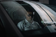 αρσενικός μυστικός αξιωματούχος στα γυαλιά ηλίου που κάθεται στο αυτοκίνητο με το φλιτζάνι του καφέ εγγράφου κάνοντας στοκ φωτογραφίες αρσενικός μυστικός αξιωματούχος στα γυαλιά ηλίου που κάθεται στο αυτοκίνητο με το φλιτζάνι του καφέ εγγράφου κάνοντας στοκ φωτογραφίες