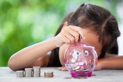 Ασιατικό κορίτσι που κάνει τους σωρούς των νομισμάτων και που βάζει τα χρήματα στη piggy τράπεζα στοκ εικόνες Ασιατικό κορίτσι που κάνει τους σωρούς των νομισμάτων και που βάζει τα χρήματα στη piggy τράπεζα στοκ εικόνες