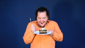 Αστείο παχύ άτομο στο πορτοκαλί πουκάμισο με ένα κομμάτι του κέικ σοκολάτας σε ένα πιάτο φιλμ μικρού μήκους Αστείο παχύ άτομο στο πορτοκαλί πουκάμισο με ένα κομμάτι του κέικ σοκολάτας σε ένα πιάτο φιλμ μικρού μήκους