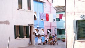 ΒΕΝΕΤΙΑ, BURANO, ΙΤΑΛΊΑ - 7 ΙΟΥΛΊΟΥ 2018: ατμοσφαιρική οδός στο νησί Burano Ο ηλικιωμένος άνθρωπος κάθεται στην οδό, κεντά απόθεμα βίντεο ΒΕΝΕΤΙΑ, BURANO, ΙΤΑΛΊΑ - 7 ΙΟΥΛΊΟΥ 2018: ατμοσφαιρική οδός στο νησί Burano Ο ηλικιωμένος άνθρωπος κάθεται στην οδό, κεντά απόθεμα βίντεο