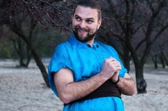 Γέλιου γύρω από το όμορφο γενειοφόρο άτομο στο μπλε κιμονό που στέκεται με τα χέρια στοκ φωτογραφία Γέλιου γύρω από το όμορφο γενειοφόρο άτομο στο μπλε κιμονό που στέκεται με τα χέρια στοκ φωτογραφία