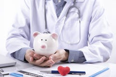 Γιατρός και piggy τράπεζα στην επιτραπέζια ιατρική αμοιβή για την υγειονομική περίθαλψη στοκ φωτογραφία με δικαίωμα ελεύθερης χρήσης Γιατρός και piggy τράπεζα στην επιτραπέζια ιατρική αμοιβή για την υγειονομική περίθαλψη στοκ φωτογραφία με δικαίωμα ελεύθερης χρήσης