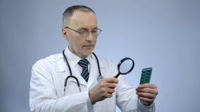 Γιατρός που εξετάζει το πακέτο των χαπιών μέσω της ενίσχυσης - γυαλί, πλαστό φάρμακο στοκ φωτογραφία με δικαίωμα ελεύθερης χρήσης Γιατρός που εξετάζει το πακέτο των χαπιών μέσω της ενίσχυσης - γυαλί, πλαστό φάρμακο στοκ φωτογραφία με δικαίωμα ελεύθερης χρήσης