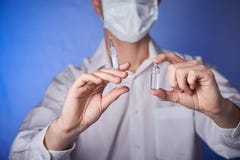 Γιατρός στη μάσκα με μια σύριγγα εγχύσεων στο μπλε υπόβαθρο στοκ εικόνες Γιατρός στη μάσκα με μια σύριγγα εγχύσεων στο μπλε υπόβαθρο στοκ εικόνες