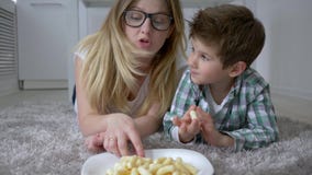 Γλυκό δόντι, μικρό αγόρι με το mum στα γυαλιά που τρώνε τα μπισκότα από το πιάτο που βρίσκεται στο πάτωμα στο δωμάτιο απόθεμα βίντεο Γλυκό δόντι, μικρό αγόρι με το mum στα γυαλιά που τρώνε τα μπισκότα από το πιάτο που βρίσκεται στο πάτωμα στο δωμάτιο απόθεμα βίντεο