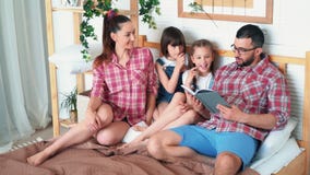 Γονείς και δύο κόρες βρίσκονται στο κρεβάτι και ο μπαμπάς διαβάζει το βιβλίο σε τους, σε αργή κίνηση φιλμ μικρού μήκους Γονείς και δύο κόρες βρίσκονται στο κρεβάτι και ο μπαμπάς διαβάζει το βιβλίο σε τους, σε αργή κίνηση φιλμ μικρού μήκους