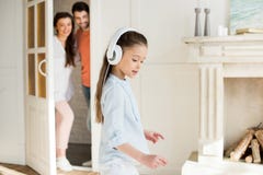 Γονείς που εξετάζουν το χαριτωμένο μικρό κορίτσι στα άσπρα ακουστικά στοκ εικόνες με δικαίωμα ελεύθερης χρήσης Γονείς που εξετάζουν το χαριτωμένο μικρό κορίτσι στα άσπρα ακουστικά στοκ εικόνες με δικαίωμα ελεύθερης χρήσης