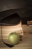 Γραφείο δασκάλων τα βιβλία που συσσωρεύονται με, Mortarboard, τη Apple και Chalkb Στοκ Φωτογραφία Γραφείο δασκάλων τα βιβλία που συσσωρεύονται με, Mortarboard, τη Apple και Chalkb Στοκ Φωτογραφία