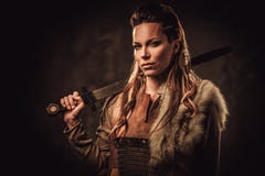 Γυναίκα Βίκινγκ με το ξίφος ενδύματα στα παραδοσιακά πολεμιστών, που θέτουν σε ένα σκοτεινό υπόβαθρο στοκ εικόνες Γυναίκα Βίκινγκ με το ξίφος ενδύματα στα παραδοσιακά πολεμιστών, που θέτουν σε ένα σκοτεινό υπόβαθρο στοκ εικόνες