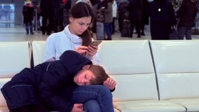 Γυναίκα με τον κουρασμένο γιο της στην αίθουσα αερολιμένων με ένα κινητό τηλέφωνο στα χέρια της που περιμένουν την πτήση απόθεμα βίντεο Γυναίκα με τον κουρασμένο γιο της στην αίθουσα αερολιμένων με ένα κινητό τηλέφωνο στα χέρια της που περιμένουν την πτήση απόθεμα βίντεο