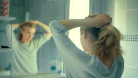 Γυναίκα που δένει τα μακριά ξανθά μαλλιά της που αντιμετωπίζουν τον καθρέφτη στο λουτρό της απόθεμα βίντεο Γυναίκα που δένει τα μακριά ξανθά μαλλιά της που αντιμετωπίζουν τον καθρέφτη στο λουτρό της απόθεμα βίντεο