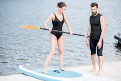 Γυναίκα που μαθαίνει να κάνει σερφ σε ένα paddleboard με τον εκπαιδευτικό στοκ εικόνα με δικαίωμα ελεύθερης χρήσης Γυναίκα που μαθαίνει να κάνει σερφ σε ένα paddleboard με τον εκπαιδευτικό στοκ εικόνα με δικαίωμα ελεύθερης χρήσης