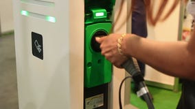 Γυναίκα που συνδέει το ηλεκτρικό αυτοκίνητο στην υποδοχή στον άνετο δημόσιο σταθμό χρέωσης Γυναίκα που συνδέει το ηλεκτρικό αυτοκίνητο στην υποδοχή στον άνετο δημόσιο σταθμό χρέωσης