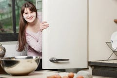 Γυναίκα στην κουζίνα που κρυφοκοιτάζει έξω από πίσω από την πόρτα ενός ανοικτού ψυγείου και που χαμογελά εξετάζοντας τη κάμερα στοκ φωτογραφίες Γυναίκα στην κουζίνα που κρυφοκοιτάζει έξω από πίσω από την πόρτα ενός ανοικτού ψυγείου και που χαμογελά εξετάζοντας τη κάμερα στοκ φωτογραφίες