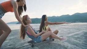 Γυναίκα τριών φίλων που χαμογελά και που οδηγά στο longboard στην παραλία στο ηλιοβασίλεμα απόθεμα βίντεο Γυναίκα τριών φίλων που χαμογελά και που οδηγά στο longboard στην παραλία στο ηλιοβασίλεμα απόθεμα βίντεο